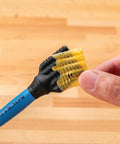 Hand holding blue handle of Silicone Glue Brush Set For Beadlock Tenons Ribbed Tenon Shaped Applicators on wooden surface.