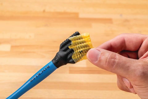 Hand holding blue handle of Silicone Glue Brush Set For Beadlock Tenons Ribbed Tenon Shaped Applicators on wooden surface.