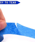 Close-up of hand tearing Blue Painter Tape Set With 1/4 In, 1/2 In, 3/4 In Widths For Pro Grade Precision on white surface
