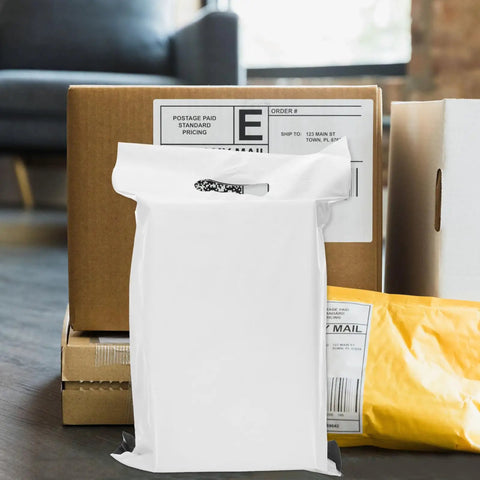 White poly mailer bag with adhesive seal standing among boxes, representing 100 Pack White Poly Mailer Bags Thickened Lightweight Envelopes.