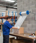 No Sweat Wall Mount Bubble Wrap Roll Dispenser With Flexible Snap Connector And Secure Side Locks For Pro Warehouse Shipping Or Heavy Weekend Moving Day Packing Jobs, in use for packing a box.