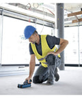 Man using Hardcore Stud Finder Wall Scanner on floor in construction site, wearing safety vest and helmet, focused on accuracy.