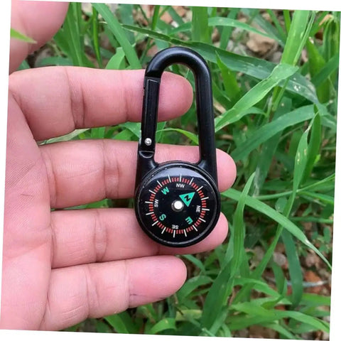 Person holding a Portable Double Sided Hiking Compass With Carabiner Pocket Sized Mini Outdoor Navigation Tool against green foliage.