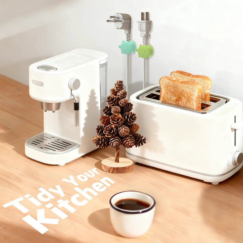 White coffee maker and toaster on wooden counter with two slices of toast, coffee cup, and decorative pinecone tree.