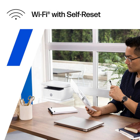 Wireless Laser Printer For Small Teams With Fast Black And White Printing Scanning And Copying Easy Setup And Mobile Printing Budget Friendly Compact MFP Built For Home Office Or Tiny Teams shown on a desk next to a man reading.
