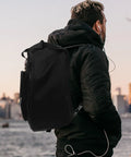 Road Ready Snare Drum Case And Gig Bag With Badass Thickened Padding And Adjustable Shoulder Strap For Smooth Hauling Of Your 14 Or 15 Inch Snare In Sleek Matte Black on a person in a cityscape.