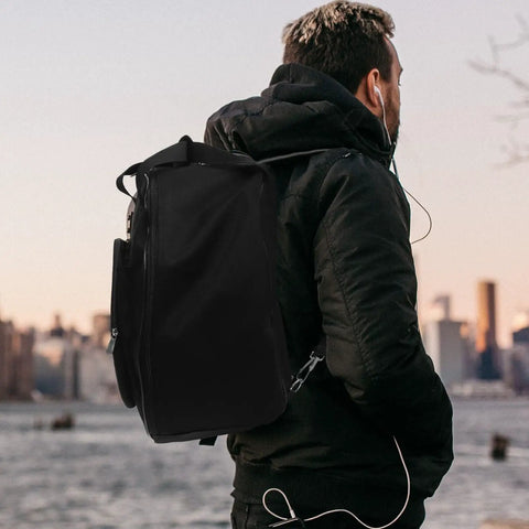 Road Ready Snare Drum Case And Gig Bag With Badass Thickened Padding And Adjustable Shoulder Strap For Smooth Hauling Of Your 14 Or 15 Inch Snare In Sleek Matte Black on a person in a cityscape.