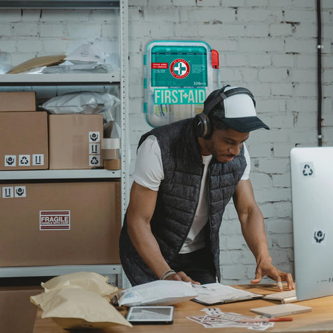 First aid kit, teal, 326-piece Be Smart Get Prepared; wall-mounted with man at desk wearing headphones.