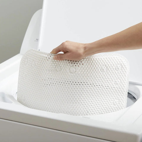 Person placing Softex Bath Mat For Tubs 17 By 36 Inches Taupe Machine Washable Skid Resistant with Suction Cups into washing machine
