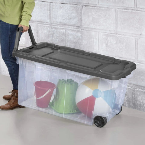 Rugged Pull Along 160 Quart Rolling Storage Tote With Transparent Bottom, holding colorful beach toys, on wheels.