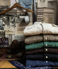 Stack of folded shirts with pearl snap buttons in a rustic, decorative setting with vintage photos and artifacts.