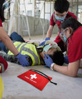 Red zippered first aid kit pouch with white cross and FIRST AID KIT text on a construction-site floor.