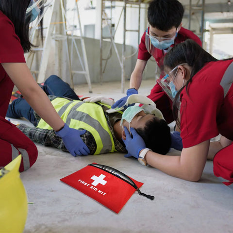 Red zippered first aid kit pouch with white cross and FIRST AID KIT text on a construction-site floor.