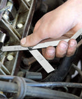 Close-up of hand using a two-piece steel feeler gauge with dual metric and imperial blades to measure an engine gap