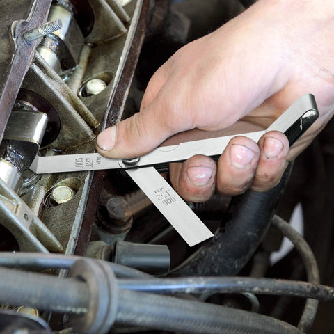 Close-up of hand using a two-piece steel feeler gauge with dual metric and imperial blades to measure an engine gap