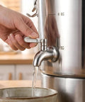 Hand operating the spigot of a Straight Up Heavy Duty 304 Stainless Steel Beverage Dispenser pouring liquid into a bowl.