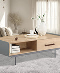 Lightwood coffee table in modern living room with vase, books, and decor on gray carpet, window in background.