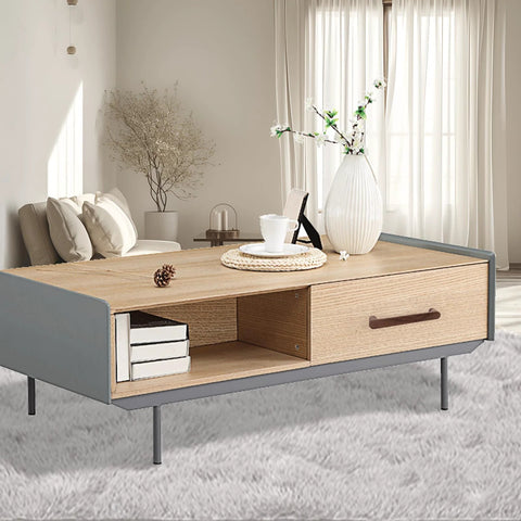 Lightwood coffee table in modern living room with vase, books, and decor on gray carpet, window in background.