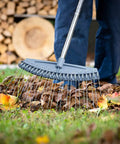 Person using Adjustable 17 To 63 Inch Thatch Rake With 24 Steel Tines to gather leaves, ergonomic handle seen in garden cleanup