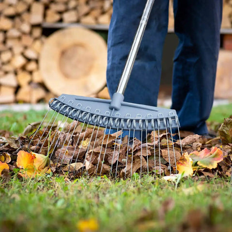 Person using Adjustable 17 To 63 Inch Thatch Rake With 24 Steel Tines to gather leaves, ergonomic handle seen in garden cleanup