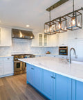 Modern kitchen with pendant lights, marble countertop, and blue island, showcasing a stylish interior.