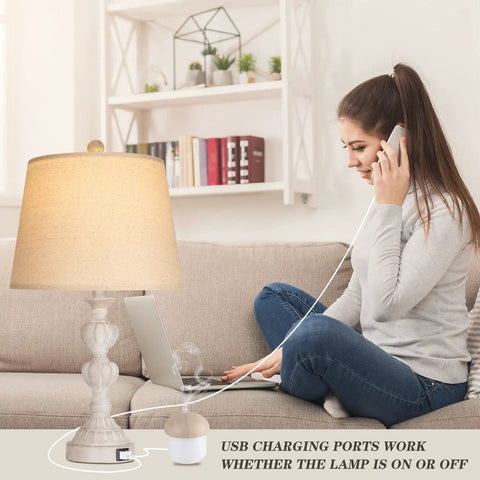 Coastal Farmhouse Table Lamp with USB port, washed white finish, beige shade, on a living room table. Woman using laptop and phone.