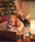 Woman relaxing with laptop near Christmas tree, next to Dual USB Charging Ports And AC Outlet Nightstand Lamps Set Of 2 Touch Control 3 Way Dimmable Bedside Lamps With ST64 E26 LED Bulbs Included Grey Fabric Cylinder Shade Great For Bedroom Or Living Room.