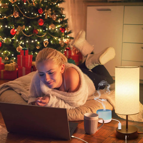 Woman relaxing with laptop near Christmas tree, next to Dual USB Charging Ports And AC Outlet Nightstand Lamps Set Of 2 Touch Control 3 Way Dimmable Bedside Lamps With ST64 E26 LED Bulbs Included Grey Fabric Cylinder Shade Great For Bedroom Or Living Room.