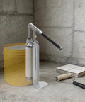 Heavy Duty Manual Loading Paste Pump With 15 Inch Handle And Stable Aluminum L Base For Thick Liquids next to a yellow bucket.