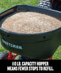 Heavy Duty 110 Lb Capacity Pull Behind Lawn Broadcast Spreader hopper filled with seed on grass, Craftsman brand visible.