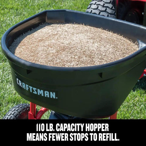 Heavy Duty 110 Lb Capacity Pull Behind Lawn Broadcast Spreader hopper filled with seed on grass, Craftsman brand visible.