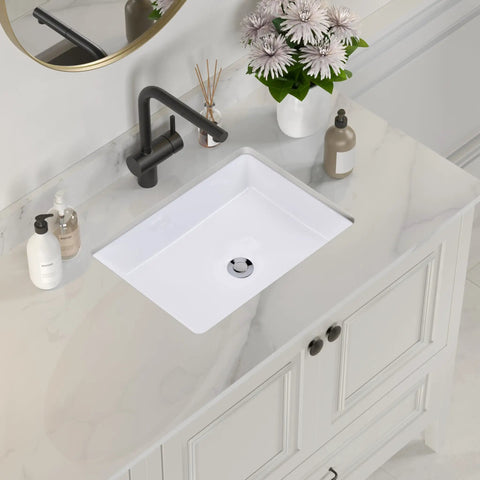Rectangular Ceramic Undermount Bathroom Sink for Vanity 20 by 16 White Vitreous China Sleek Ultra Smooth Finish With Overhang Cutout Template Exterior 19 and a Half by 15 and a Half One Year Limited Warranty installed in a marble countertop with faucet and decor.