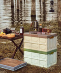 Heavy Duty Collapsible Storage Bins With Lid, Tough Camping Organizer Box For Car Trunk And Groceries, Converts To A Rock Solid Sitting Stool, 50 Liter Green Bin displayed at a campsite with drinks and snacks.