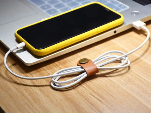 Leather Cord Organizer And Cable Keeper Case holding a wrapped charger cable beside a smartphone on a desk.