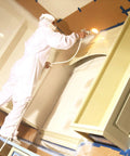 Painter using sprayer with brown general purpose masking paper 12 in x 180 ft for painting trim windows and doors.