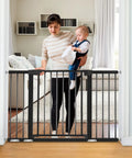 Woman holding baby next to extra wide black baby gate for stairs and doorways fits 29.93 to 51.5 inches 30 inches high