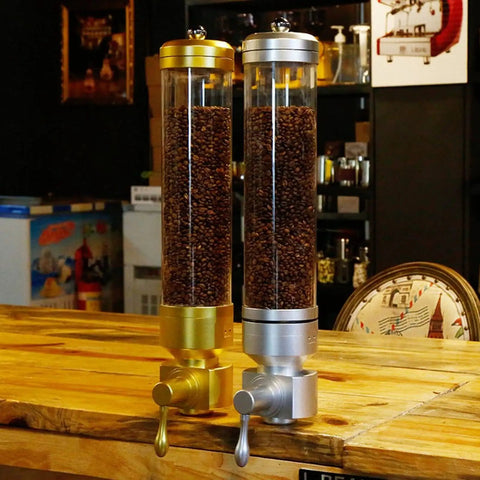 Sick Wall Mount Coffee Bean Dispenser Heavy Hitter Acrylic Canister for storing beans in gold and silver finish on a wooden table.