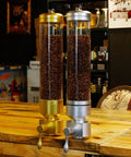Wall Mounted Coffee Bean Dispenser With Clear Acrylic Jar For Busy Cafes And Brew Spots Detachable Sealed Hopper Keeps Beans Fresh No Fuss Wipe Down Large 5100g Spot Ready Setup in gold and silver on a wood counter.