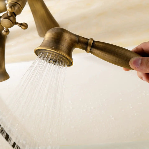 Close-up of hand using Antique Vintage Brass 6 Inch Centers Two Handle Clawfoot Bathtub Faucet Set With Deck Mounted Shower Combo Hand Shower Included, Retro Vibe, Wall Mount, Antique Brass Finish, 1.8 GPM, Two Holes, showing water flow.