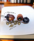 Hella Slick Screw Open Miniature Black Ebony Acorn Curios Set Of Two With Hidden Antique Bronze Pinecones on a book.