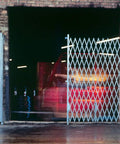 Top Shelf Double Folding Gate Extends To 14 Feet Wide With Heavy Steel Rolling Casters And Smooth Pivot Action positioned at an open warehouse entrance with a vehicle approaching.
