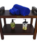 Teak Shower Bench With Shelf And LiftAide Arms For Safe Shower Mobility Adjustable Foot Pads Durable Solid Teak Bath Bathroom Bench With Drainage Slats Brown, view with towels and bottles on shelves.