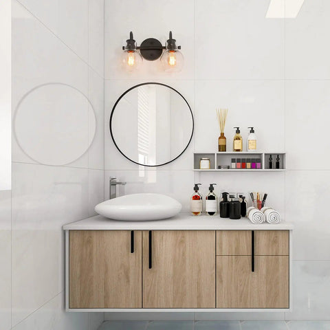 Bathroom with Black 2-Light Vanity Light Fixture With Clear Glass Shades above a round mirror and wooden vanity.