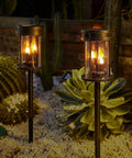 Outdoor Solar Stake Lights With Flickering Candle Lanterns For Yard And Patio 2 Pack Black Garden Pathway Lights Weatherproof 3 In 1 Design Easy Install Adds Warm Ambient Glow To Lawn Walkway Wall Decor illuminating a garden at night.