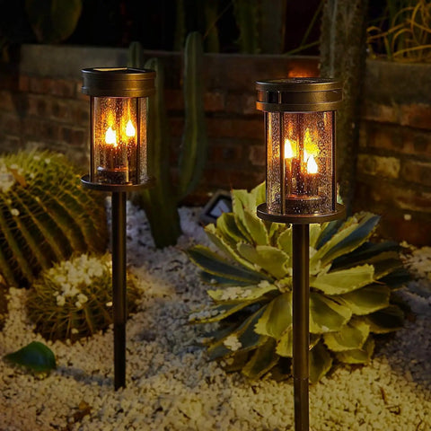 Outdoor Solar Stake Lights With Flickering Candle Lanterns For Yard And Patio 2 Pack Black Garden Pathway Lights Weatherproof 3 In 1 Design Easy Install Adds Warm Ambient Glow To Lawn Walkway Wall Decor illuminating a garden at night.