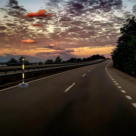 Heavy Duty Elastic Warning Bollard Post With Rock Solid Bounce Back Shield positioned on an empty road at sunset.