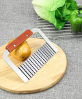 Crinkle-cut French fry slicer with stainless steel blade and wooden handle on a round cutting board