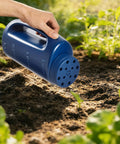 Person using blue Handheld Seed Shaker And Spreader With 90 Oz Capacity, Three Adjustable Openings for lawn care in a garden.