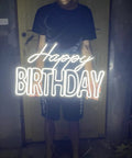 Person holding a Big Birthday Neon Sign For Wall Decor With Dimmer Switch, glowing white light on a dark background.