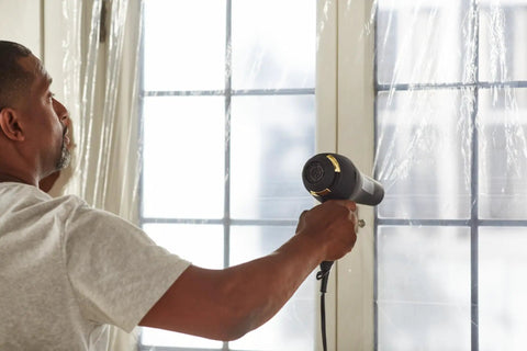 Person using hairdryer on Winter Window Insulation Kit With Roll Shrink Film That Covers Up To 15 Windows Measuring 3 By 5 Feet Tape Included No Brainer Easy Install Clear Draft Blocker For Energy Savings No Measuring Needed 15 Pack.